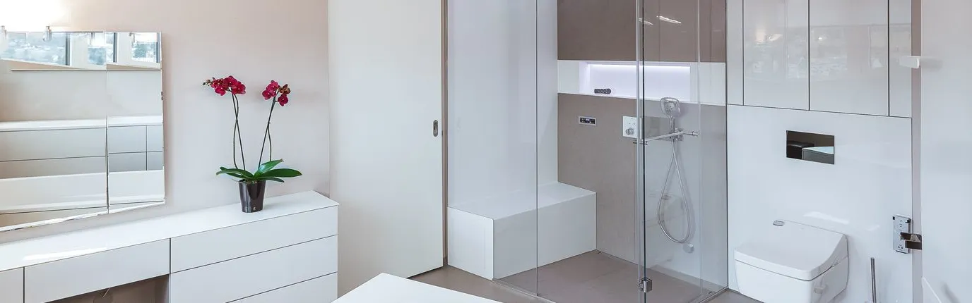 Modernes, helles Badezimmer mit weißer Kommode, Orchidee, großer Spiegel, verglaster Dusche mit Sitzbank und moderner wandhängender Toilette.