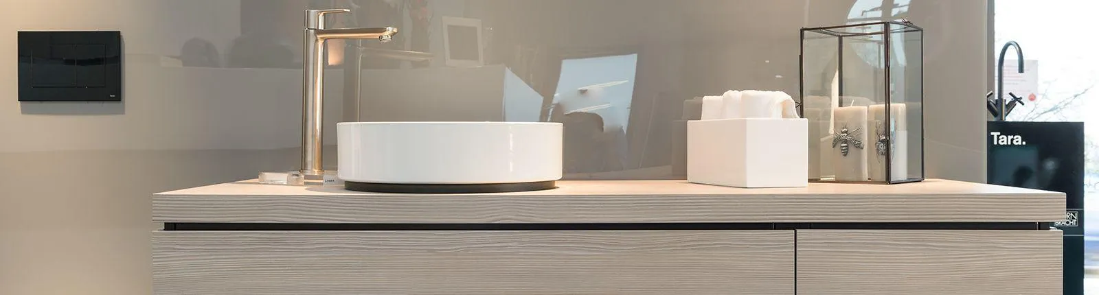 Ein modernes Badezimmer-Waschbecken mit runder, weißer Keramikschale steht auf einer hellen Holzkommode mit klarer Maserung. 