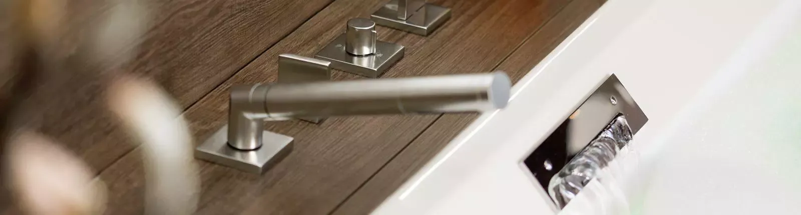 Detailaufnahme einer modernen Badewannenarmatur mit gebürstetem Edelstahlfinish und eckigem Design.