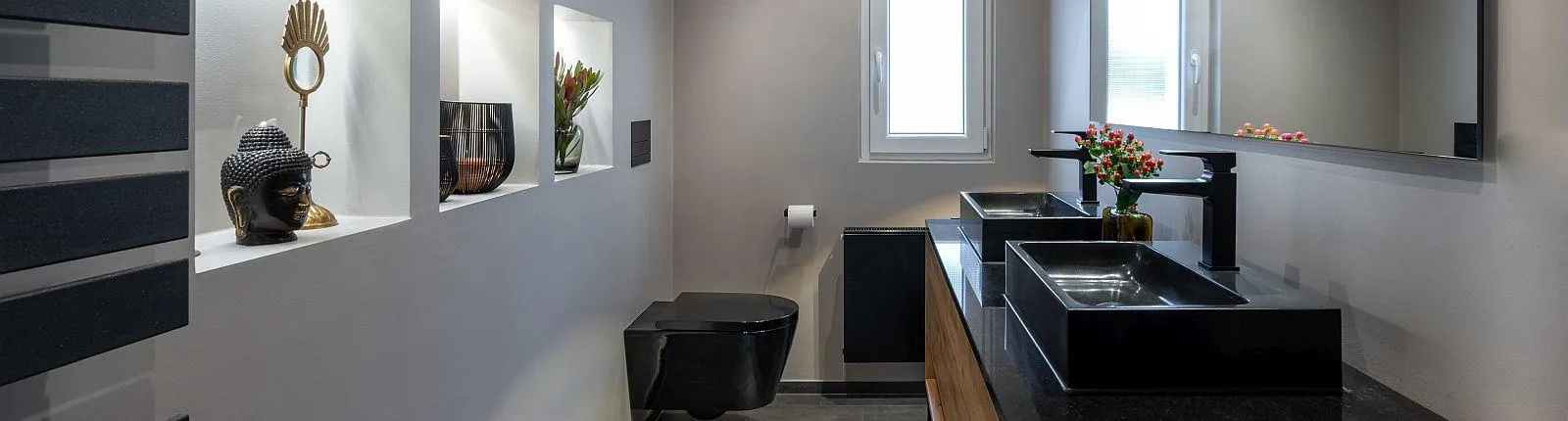 Modernes, längliches Badezimmer mit schwarzem WC, Doppelwaschtisch, dekorativen Wandnischen und großen Spiegeln.