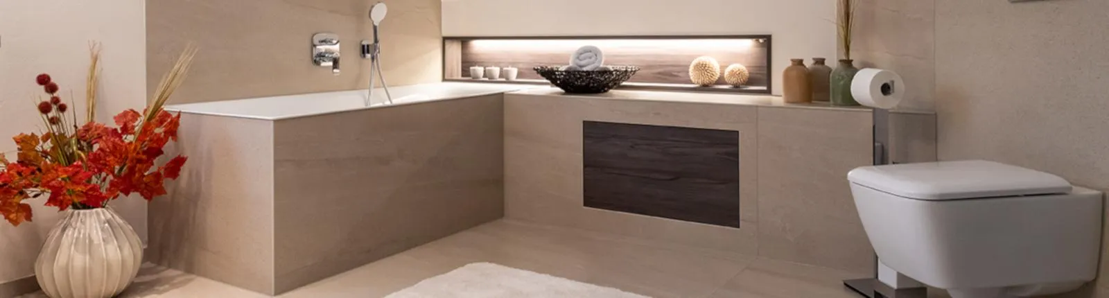 Ein elegantes Badezimmer mit beige gefliester Eckbadewanne und stilvoller Wandnische mit indirekter Beleuchtung. 