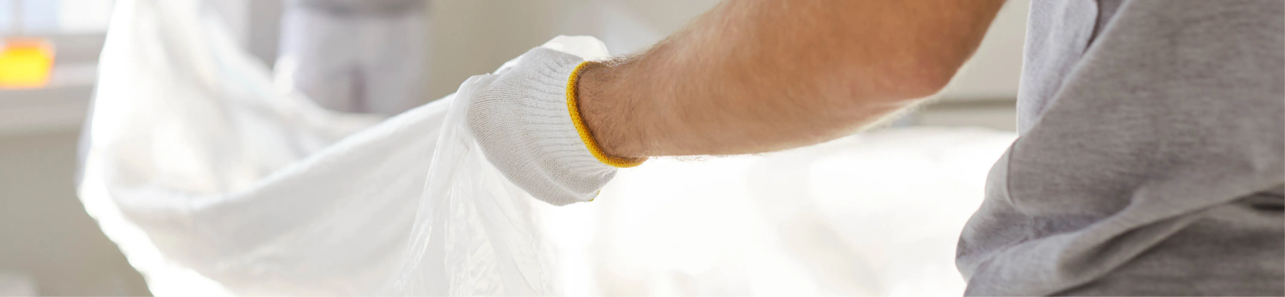 Zwei Handwerker mit Handschuhen breiten zum Staubschutz eine Plane in einem Raum aus.