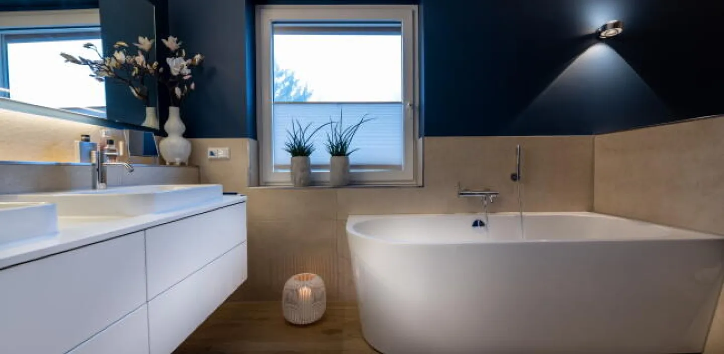 Ein modernes Badezimmer mit freistehender Badewanne und schwebendem Waschbecken, gestaltet in Weiß mit kontrastierenden dunkelblauen Wänden.