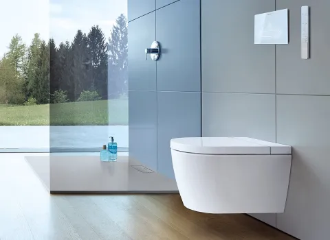 Modernes Badezimmer mit wandmontiertem Dusch-WC, großen Glasfenstern und Blick ins Grüne. 