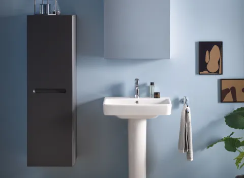 Stilvolles Bad mit Säulen-Waschtisch, schwarzem Schrank, Handtuchhaken und minimalistischer Kunst an hellblauer Wand. Schlichte, moderne Einrichtung.
