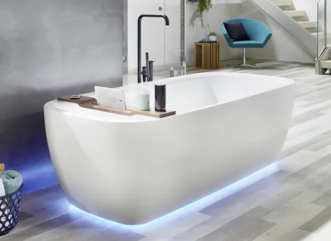 Die Whirlwanne Mauersberger ist in einem hellen Badezimmer platziert und bietet mit ihrer weichen, abgerundeten Form und der dezenten blauen LED-Beleuchtung am Boden ein luxuriöses Badeerlebnis.