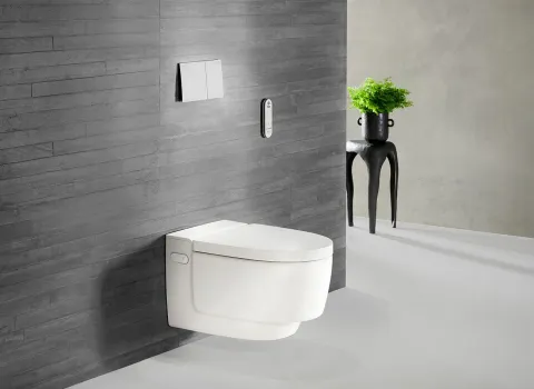 Dusch-WC AquaClean Mera Comfort mit weißer Abdeckung vor dunklen Wandfliesen. 