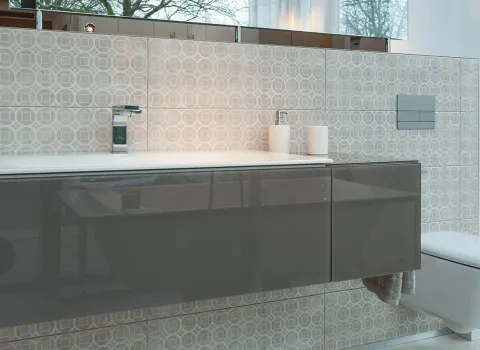 Ein elegantes Badezimmer mit wandhängendem Waschtisch in hochglänzendem Grau vor einer gefliesten Wand mit geometrischem Muster. 