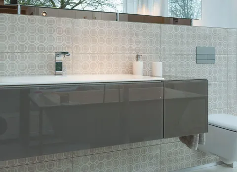 Ein elegantes Badezimmer mit wandhängendem Waschtisch in hochglänzendem Grau vor einer gefliesten Wand mit geometrischem Muster. 