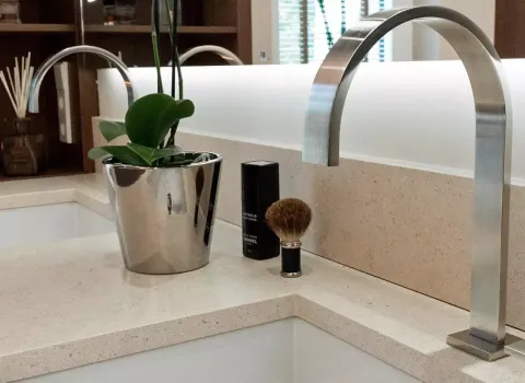 Moderner Doppelwaschtisch mit eleganten Edelstahlarmaturen, einer stilvollen Zimmerpflanze in einem glänzenden Übertopf, Rasierset und luxuriösen Pflegeprodukten – ein harmonisch eingerichtetes Elternbad