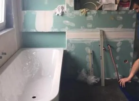 Ein Badezimmer befindet sich im Rohbau mit bereits eingebauter Badewanne und grünem Feuchtraum-Gipskarton an den Wänden.