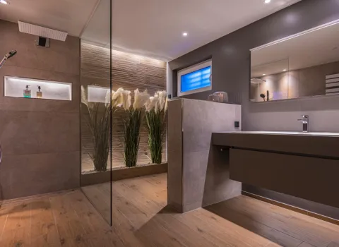 Ein luxuriöses Badezimmer mit bodengleicher Regendusche und stilvoller Holzoptik am Boden verströmt eine warme, einladende Atmosphäre.