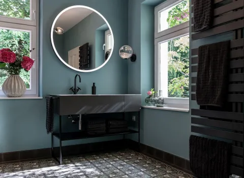 Ein stilvoll eingerichtetes Badezimmer mit rundem LED-Spiegel über einem schwebenden Waschtisch in dunklem Design.