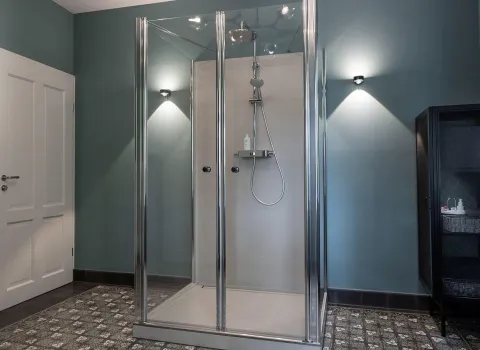 Ein modernes Badezimmer mit einer eckigen Glasdusche und großer Regendusche auf weißer Duschwand.