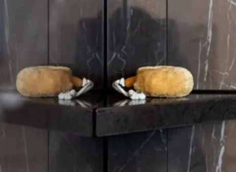 Ein eleganter Duschbereich mit dunklen Marmorfliesen zeigt eine Naturbürste, die auf einem schmalen schwarzen Eckregal liegt.