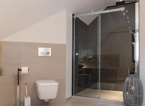 Ein modernes Badezimmer unter einer Dachschräge mit wandhängendem WC und begehbarer Dusche mit Glasfront. 