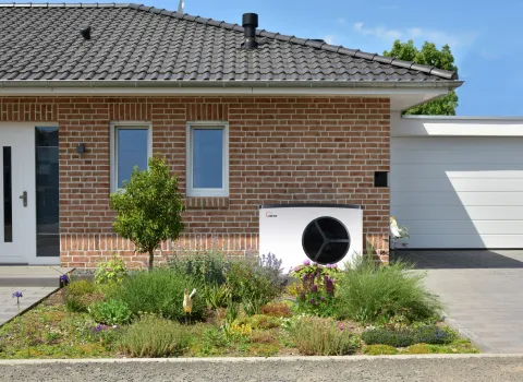 Wärmepumpe SolvisMia vor einem Einfamilienhaus aus Ziegeln mit Vorgarten.
