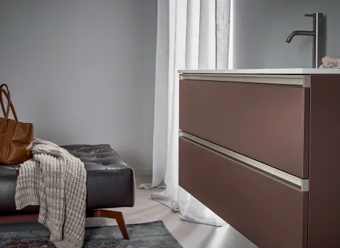 Detail eines Stocco Badmöbels mit brauner Front, integrierter Griffleiste und weißer Waschtischplatte in wohnlichem Ambiente.