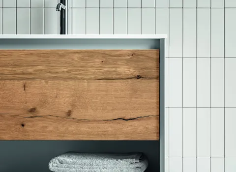 Detailansicht des Waschtischs Stocco Iks Up mit weißem Rahmen und heller Front in natürlicher Holzoptik vor weißen Fliesen.