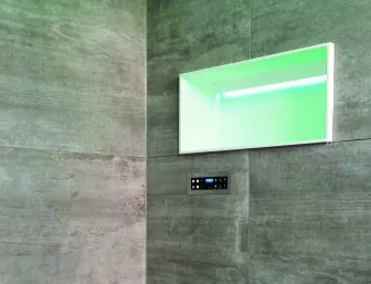 Das Bild zeigt einen Wellnessbereich mit einer Sitzbank und Wänden in Betonoptik, die dem Raum ein modernes und minimalistisches Ambiente verleihen. In die Wand ist eine beleuchtete Nische eingelassen, die in einem dezenten Grün schimmert.