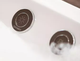 Detailaufnahme zweier runder Bedienknöpfe an einer Duravit-Whirlwanne, einer davon mit einem Sonnen-Symbol zur Steuerung der Beleuchtung.