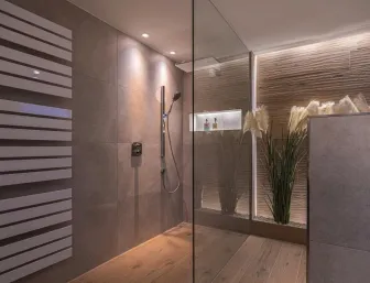 Ein modernes Badezimmer mit offener, bodengleicher Dusche, ausgestattet mit Regenduschkopf und eleganter Wandnische für Pflegeprodukte.