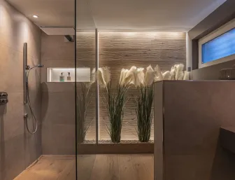 Ein stilvoll gestaltetes Badezimmer mit bodentiefer Dusche und integrierter Nische für Pflegeprodukte.