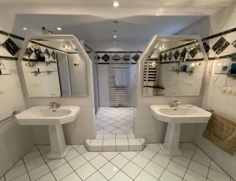 Ein Badezimmer im Retro-Stil mit zwei freistehenden Waschbecken und auffälligen, sechseckigen Spiegeln mit integrierter Beleuchtung.