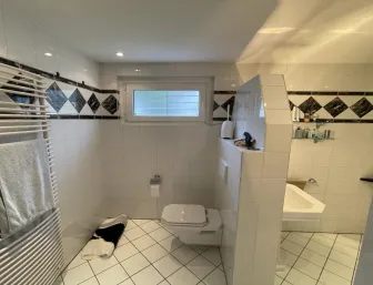 Ein klassisch gefliestes Badezimmer mit weißem Wand-WC und umlaufendem Dekorband aus schwarzen Rautenfliesen. 