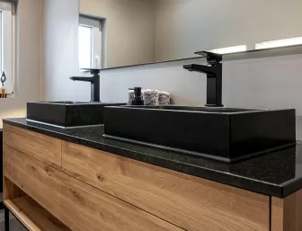 Moderner Doppelwaschtisch mit schwarzen Aufsatzbecken, schwarzen Armaturen und Waschtischunterschrank aus Holz.