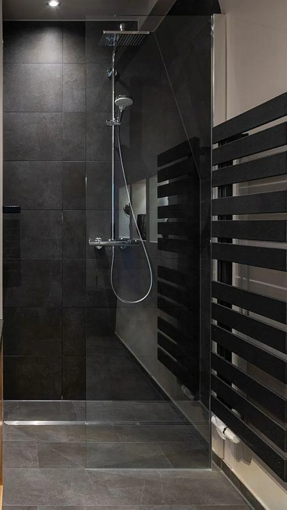 Begehbare Dusche mit dunklen Fliesen, Regendusche und modernem Handtuchheizkörper in einem renovierten Bad.
