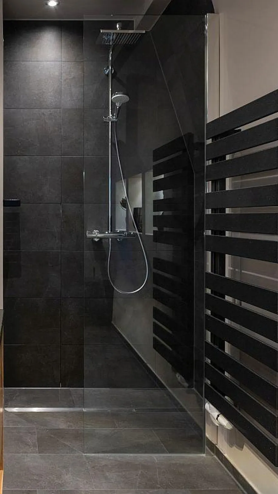 Begehbare Dusche mit dunklen Fliesen, Regendusche und modernem Handtuchheizkörper in einem renovierten Bad.