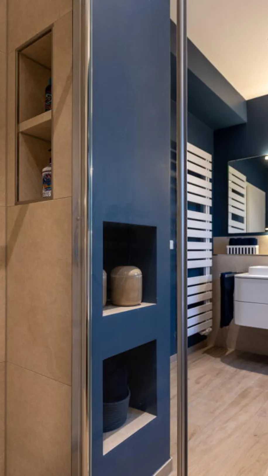 Ein modernes Badezimmer mit integrierten Wandnischen in beiger Fliesenoptik und dunkelblauer Wandfarbe. 