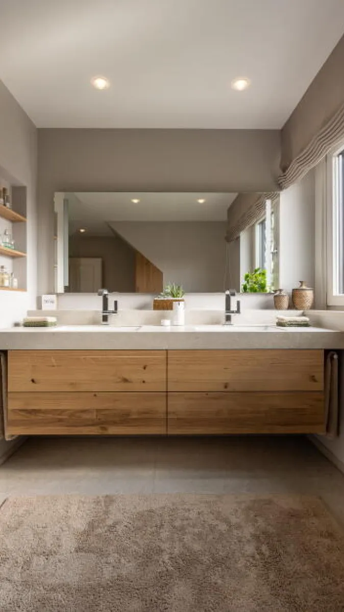 Ein modernes Badezimmer mit schwebendem Doppelwaschbecken aus Naturstein und Holzschubladen dominiert das Bild.
