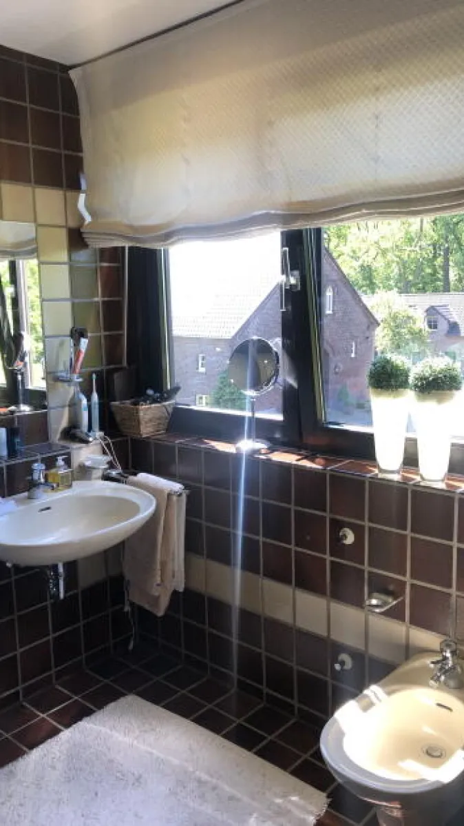 Ein Badezimmer mit retro-inspirierten, dunkelbraunen Fliesen an Wänden und Boden, die durch eine beige Zierfliesenreihe unterbrochen werden. 