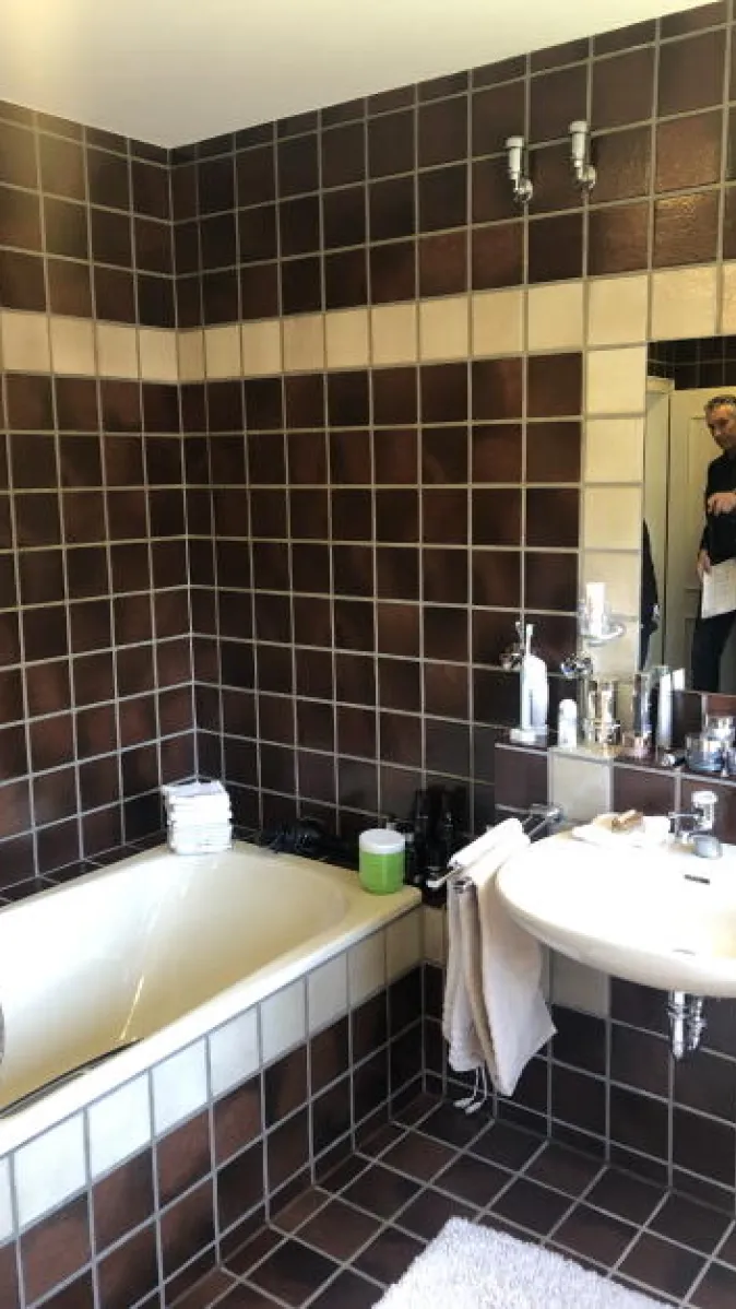 Das Bild zeigt ein Tageslichtbad mit braunen Wandfliesen im 70er-Jahre-Stil, ausgestattet mit zwei Waschbecken und einem Bidet.