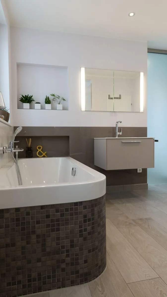 Ein modernes Badezimmer mit halbrunder Badewanne, die mit dunklen Mosaikfliesen verkleidet ist.