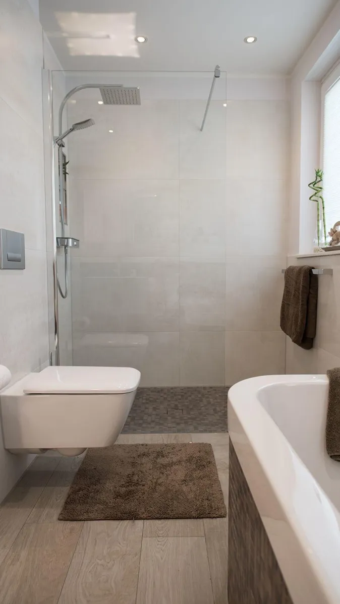 Ein modernes Badezimmer mit begehbarer Dusche, wandhängendem WC und einer Badewanne mit Mosaikverkleidung.