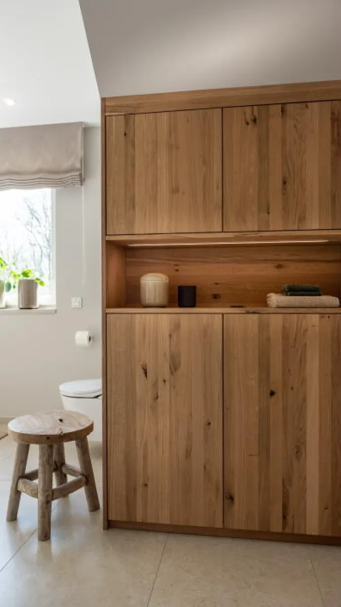 Ein Badezimmer mit einem hohen Holzschrank aus naturbelassener Eiche, der für viel Stauraum sorgt.