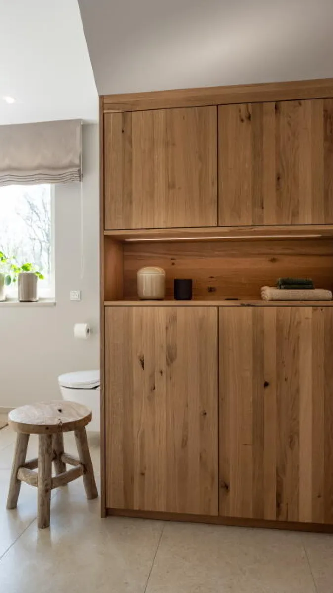 Ein Badezimmer mit einem hohen Holzschrank aus naturbelassener Eiche, der für viel Stauraum sorgt.