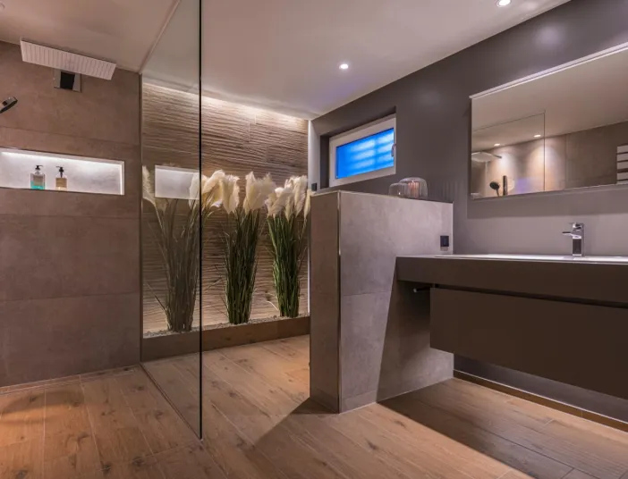 Ein luxuriöses Badezimmer mit bodengleicher Regendusche und stilvoller Holzoptik am Boden verströmt eine warme, einladende Atmosphäre.