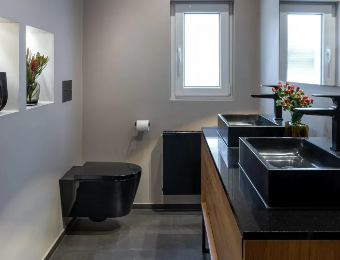 Modernisiertes Bad mit schwarzem WC, Doppelwaschtisch mit schwarzen Aufsatzbecken, dekorativen Wandnischen und minimalistischer Gestaltung.
