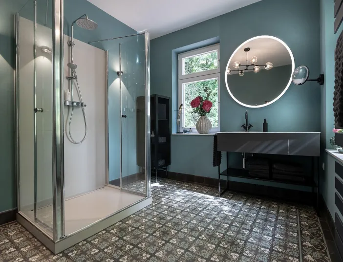 Ein luxuriöses Badezimmer mit großer Glasdusche, rundem LED-Spiegel und freischwebendem Waschtisch.