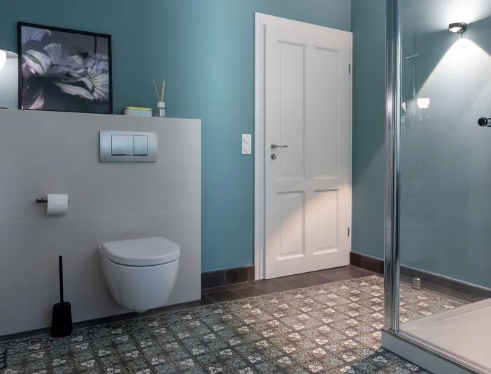 Ein modernes Badezimmer mit wandhängendem WC, Glasdusche und dekorativem Fliesenboden in floralen Mustern.