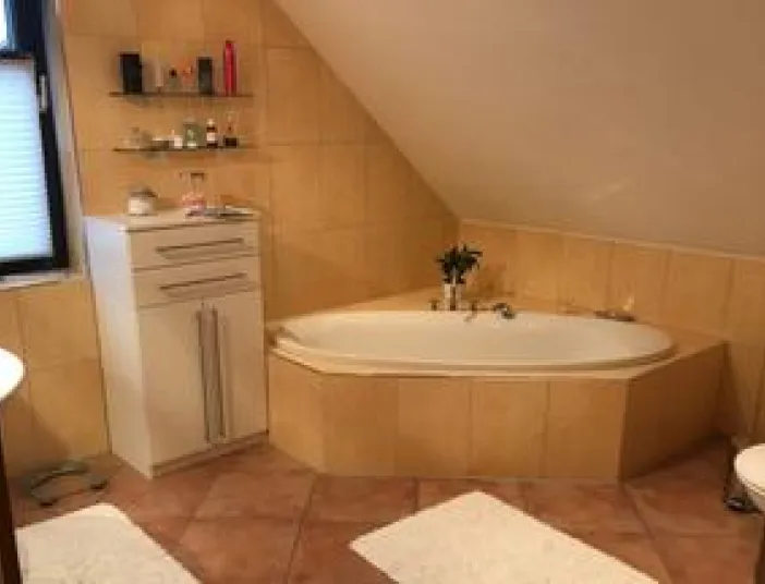 Ein gemütliches Badezimmer mit Eckbadewanne unter der Dachschräge, umgeben von beigen Fliesen.