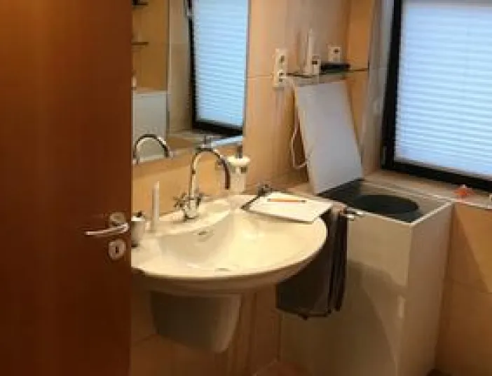 Ein kompaktes Badezimmer mit wandmontiertem Waschbecken und großer Spiegelfläche über dem Waschplatz. 