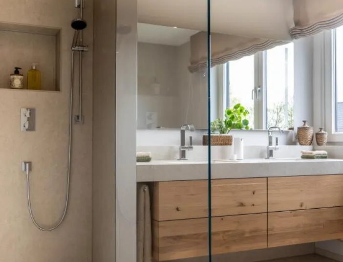 Ein modernes Badezimmer mit einer offenen Dusche links und einem Doppelwaschbecken aus Naturstein rechts.