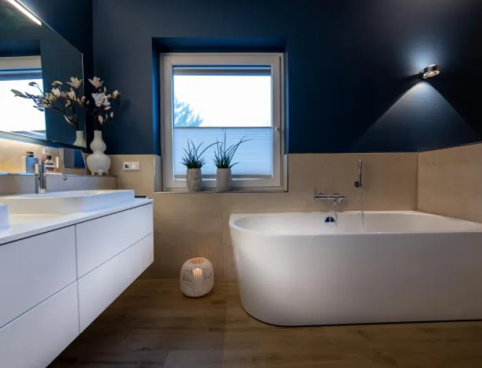 Ein modernes Badezimmer mit freistehender Badewanne und schwebendem Waschbecken, gestaltet in Weiß mit kontrastierenden dunkelblauen Wänden.