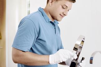 Junger Monteur montiert eine Armatur mit weißen Handschuhen